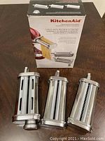Three chrome-plated cylindrical attachments laid in front of original box on wooden surface