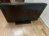 Sony Bravia flat screen TV with black frame and built-in stand photographed on wooden floor.