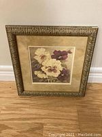 Frontal view of framed floral wall art with visible chip on top right corner and scratches on frame.