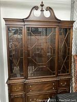 Front view of dark wood antique curio cabinet with carved details and glass paneled doors