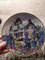Front side of the limited edition decorative plate showing the artwork of two children picking flowers in front of a rustic house.