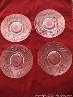 Four clear crystal dessert plates with pinwheel and diamond cut pattern displayed on red cloth, showing starburst design in center.