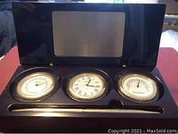 Closed view of the wooden desk set featuring three instruments (clock, thermometer, hygrometer) and a pen resting below them.