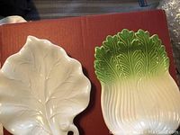 White ceramic leaf-shaped decorative plate on reddish surface.
