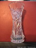 Clear crystal vase with detailed pinwheel cut pattern shown from front on a reddish-brown background.
