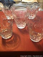 Five clear pinwheel pattern crystal glasses arranged on a red surface showing exterior cut design and one glass with a chip on the rim.
