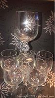 Set of six crystal wine glasses arranged with one glass elevated showing faceted rounded stem detail and clear bowl