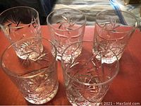 Five clear crystal drinking glasses arranged showing the pinwheel cut starburst design near the bowl.