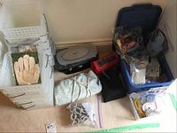 Photo shows plastic storage baskets, pairs of gloves, assorted sewing supplies in boxes and zip bags, curlers, and heating pad.