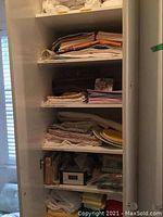 Photo of a cabinet with multiple shelves containing folded linens including tablecloths, placemats, napkins, and towels.