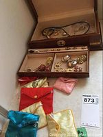 Overhead view of wooden box with open lid showing top tray contents, jewelry pouches arranged below