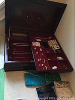 Open wooden jewelry box showing red velvet interior trays and assorted necklaces