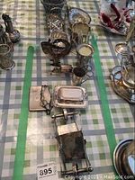 Wide view of various silver plated pieces arranged on checked tablecloth