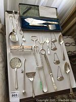 Top view of entire assortment laid out on white background, including boxed fish server set, forks, spoons, tongs, bottle labels