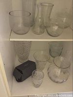Shelf with various clear glass vases of different shapes and sizes including a boxed Waterford crystal vase.