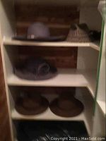 Shelf with six ladies hats: beige wool hat with rope trim, pink sun hat with flower accent, two brown wide brim hats, two tweed style hats.