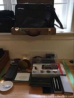 Photo of desk accessories including pen sets, brass shell bookends, stapler, battery organizer/tester, calculator, paperweight, coin trays, and a leather briefcase and wooden briefcase.