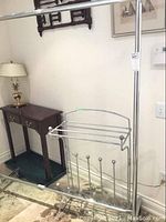 Photo of the large metal clothing rack on wheels positioned near a wall with a lamp and small table in the background.