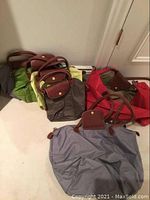 Overview of six nylon bags in red, taupe, grey, light green, chartreuse and olive tones arranged on floor
