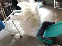 Stack of approx. 20 clear plastic storage boxes with lids alongside metal cart and Rubbermaid tub
