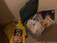 Overview of lot showing yellow raincoat on hanger, plastic bin with children’s books, utensils, cups, and bath toys inside