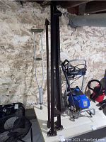 Photo showing two tall brown metal vertical bed frame posts with flat feet plates and crutch visible in background.