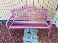 Front view of red metal bench with bird and leaf decorative backrest, showing wear and rust.