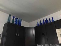 Overview of blue glass bottles and vases displayed on top of dark cabinetry, showing variety in shapes and sizes.