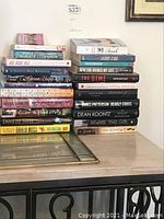 Stack of assorted books by Dean Koontz, Nora Roberts, Ivanka Trump, and others on a table.