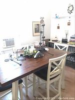 Photo showing dining table with all metal candle holders and napkin holder arranged on top, background includes chairs and wall art