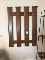 Full view of the wood wall-mounted coat and hat rack with four vertical panels and brass hooks