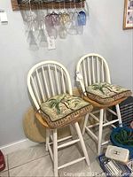 Two white swivel counter height wooden chairs with patterned cushions, round stone top visible beside them.