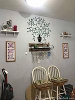 Wall with metal tree wall art, framed photographs, two chairs with cushions, a hanging glass rack with glassware, and shelves with various items.
