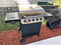 Front view of Char-Broil 6 burner gas grill, showing stainless steel lid, control knobs, and left side burner with flat shelf area.