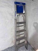 Full view of the folded 6-foot aluminum Werner ladder leaning against a textured white wall.