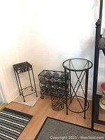 Photo of two metal plant stands, metal magazine rack, and small metal container arranged on floor near wall