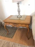 Full view of wooden side table with glass top and lamp on top