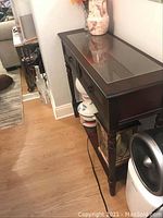 Side view of a dark wooden side table with drawer handles and a reflective top surface.