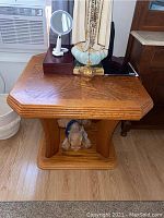 Front view of wooden side table showing octagonal top, beveled edges, and curved legs over a rectangular base with a plush toy beneath.