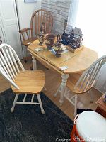 Photo showing wooden kitchen table with three chairs around it and various decorative items on table.