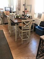 Full view of the dining table and chairs set inside a room showing the wood top table with white legs and four chairs around it.