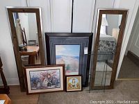 Photo showing one large framed nature print, one floral cottage painting, one small circular artwork with lady and bunny, two wooden framed mirrors - one wide door mirror and one narrow mirror.