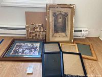 Overview of lot including framed religious art, framed soldiers art, cork board made of wine corks, and several wooden picture frames on floor.
