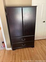 Closed dark brown wooden wardrobe with two drawers and silver handles