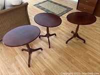 Three Bombay fold-down side tables in dark wood finish arranged on a wooden floor showing varying sizes and shapes.