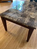 Close-up side view showing marble-look top and wooden tapered legs of an end table.