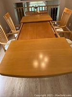Photo showing the rectangular solid wood dining table with the top partially removed, four wooden chairs around the table, and the natural wood finish visible.