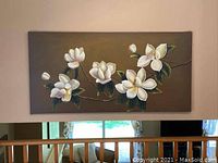 Photo of a stretched canvas painting depicting white magnolia flowers with green leaves on a brown background, hung on a wall.