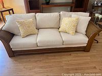 Front view of wicker sofa with cream cushions and two yellow throw pillows