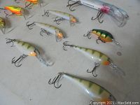 Photo showing assortment of minnow-shaped fishing lures with white/silver bodies and green/orange accent colors, each with treble hooks.